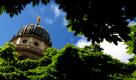 Der Französische Dom auf dem Gendarmenmarkt in Berlin ragt von grünen Blättern umrahmt in den blauen Himmel.  Foto: dpa