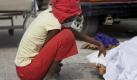 Eine Frau hebt auf einem Parkplatz in Port-au-Prince das Laken, mit dem eine Leiche bedeckt ist. Foto: dpa
