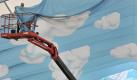 Ein Mann auf einer Hebebühne befestigt auf dem Oktoberfestgelände in München hellblaue Stoffbahnen mit Wolkenmotiven am Dach eines Bierzeltes. Foto: Peter Kneffel, dpa Foto: dpa