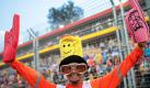 Beim Großen Preis von Singapur können selbst die Streckenposten ihre Liebe zur Formel 1 nicht verbergen. Dieser hat sich mit Winkpappe und Smileyhut vor einer Tribüne positioniert. Foto: dpa/Jan Woitas