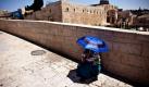 Eine Bettlerin schützt sich in Jerusalem mit einem Regenschirm vor der Sonne.  Foto: ap