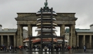 Touristen betrachten in Berlin vor dem Brandenburger Tor die Installation At Crossroads der griechischen Künstlerin Kalliopi Lemos. Der 13 Meter hohe Turm aus neun Holzbooten von Flüchtlingen aus dem Nahen Osten wird bis zum 30. Oktober in Berlin ausgestellt. Foto: ddp