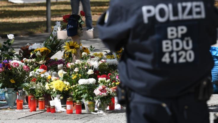 Bei einer Gedenkveranstaltung am Tatort in Chemnitz steht ein Polizist neben den Blumen.