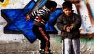 Zwei palästinensische Kinder spielen vor einer von Mitgliedern der Hamas bemalten Mauer. Die Zeichnung zeigt eine Hand, die mit einem Messer auf einen Davidstern einsticht. Foto: dpa