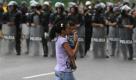 Die Fronten in Venezuela sind verhärtet. Eine Frau passiert mit ihrem Baby eine Polizeieinheit, die am Rande einer Oppositionsdemonstration aufmarschiert ist. Foto: ap