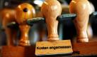 Ein Stempel mit der Aufschrift Kosten angemessen hängt in einem Gericht in Köln im Stempelkarussell. Die Bundesregierung hat das größte Sparpaket in der bundesdeutschen Geschichte beschlossen. Bis Ende 2014 wollen Union und FDP im Bundeshaushalt 81,6 Milliarden Euro einsparen - vor allem bei Arbeitslosen, Familien und im öffentlichen Dienst. Foto: dpa