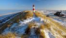 Auch im Winter reizt das Meer und bietet wunderbare Aussichten. So wie hier auf Sylt. Zu sehen sind die typischen Reetdachhäuser und der Leuchtturm am Ellenbogen vor verschneiten Dünen.  Foto: dpa