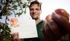 Jork, Niedersachsen. Axel Schuback posiert auf seiner Obstplantage mit einer Patenschaftsurkunde und Äpfeln neben einem Apfelbaum. Der Landwirt vergibt jedes Jahr rund 2000 Baumpatenschaften, die Paten erhalten eine Urkunde und dürfen nach Belieben Äpfel ernten. Foto: dapd