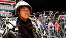 Ein thailändischer Soldat patrouilliert entlang eines abgesperrten Bereichs in der Hauptstadt Bangkok. Im Hintergrund sind Demonstranten zu sehen, die die Regierung unterstützen und somit den regierungskritischen Rothemden die Stirn bieten.  Foto: dpa