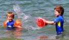 Toben im Wasser ja, aber bitte mit Neoprenanzügen: Lucas (rechts) und Benjamin planschen am Ostseestrand von Warnemünde bei einer Lufttemperatur von 20 Grad. Das Wasser hat dort inzwischen knapp 18 Grad erreicht. Foto: dpa
