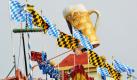 Fahnen wehen auf dem Oktoberfestgelände in München vor einem übergroßen Bierkrug eines Bierzelts. Am 18. September heißt es wieder: O'zapft is! Bis zum 3. Oktober feiert das größte Volksfest der Welt dann sein 200-jähriges Jubiläum. Foto: dpa