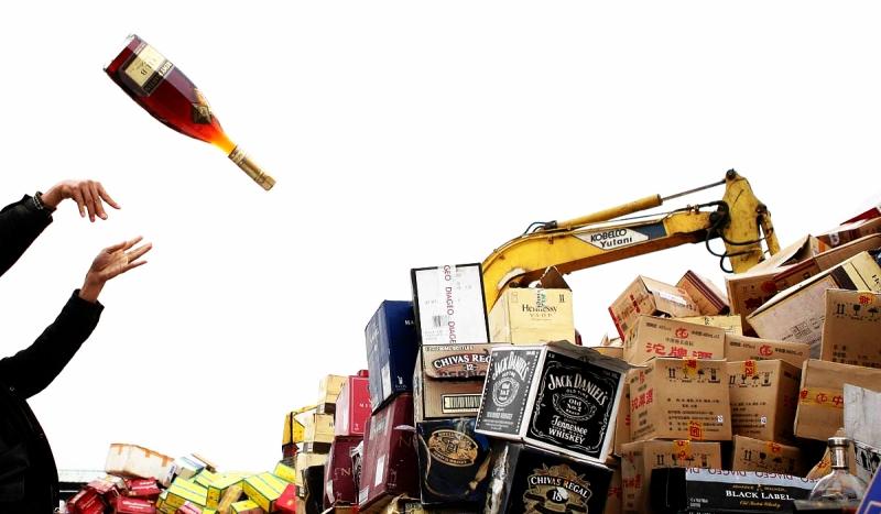 Ein Mann in Südchina wirft eine Flasche Alkohol auf einen Berg Kisten, der später zerstört wird. Dies geschieht im Rahmen einer Aktion gegen Plagiate. Foto: ap