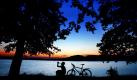 Ein Radfahrer sitzt nach Sonnenuntergang am Ufer des Möhnesees. Der Tourismus auf zwei Rädern rollt und rollt. Immer mehr Hotels stellen sich auf die Gäste mit dem Fahrrad ein. Die bekanntesten Radregionen in Nordrhein-Westfalen sind das Münsterland und der Niederrhein. Foto: dpa