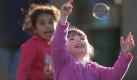 Haley Petersen (rechts) und Vanessa Ahmad jagen beim Picknick mit ihren Familien in Watertown, Wisconsin, Seifenblasen hinterher. Foto: ap