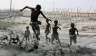 Kinder spielen in Keranigonj, Bangladesch in schlammigem Wasser, das in ein Feld gepumpt wird. Foto: ap
