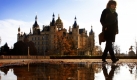 Eine Frau geht an einer Pfütze vorbei, in der sich das Schweriner Schloss spiegelt. Mit Temperaturen um die fünf Grad und einem Wechsel aus Sonne und Wolken zeigt sich der Herbst derzeit in Norddeutschland. Foto: dpa