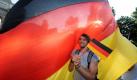 Ein Fußballfan winkt am Sonntag (27.06.2010) in München (Oberbayern) auf der Leopoldstraße mit seiner kleinen Deutschland-Fahne, während er vor einer riesigen Deutschlandfahne steht. Tausende Fußballfans feierten den Sieg der deutschen Nationalmannschaft gegen England im Achtelfinale der Fußball-Weltmeisterschaft auf der Leopoldstraße. Foto: Tobias Hase dpa/lby +++(c) dpa - Bildfunk+++ Foto: dpa