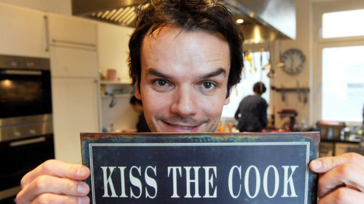 Fernseh-Koch Steffen Henssler bei der Präsentation seines neuen Kochbuchs "Hauptsache lecker!" mit einem Schild mit der Aufschrift "Kiss The Cook". (Foto)