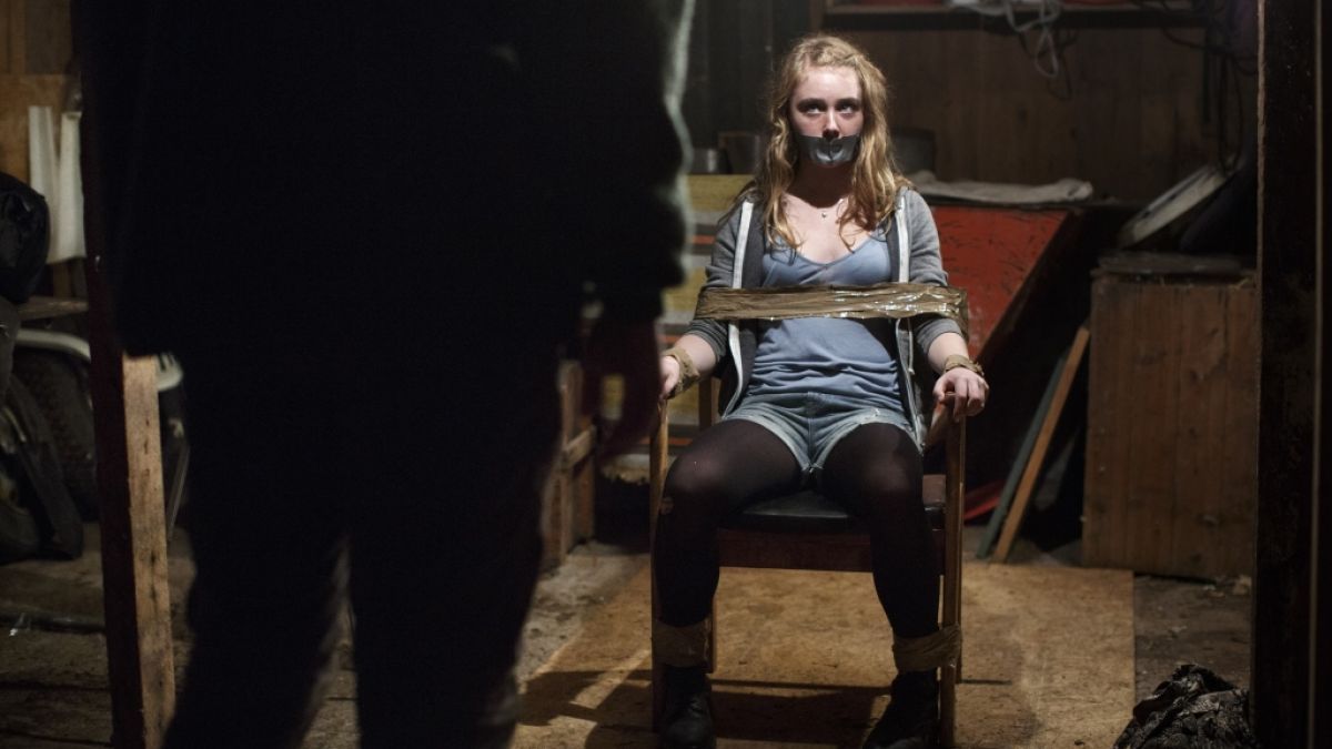 Lykke (Sara Månberg) ist mit Klebeband an einen Stuhl gefesselt und schaut einen Mann an, der ihr gegenüber sitzt. Ihr Mund ist ebenfalls mit Klebeband beklebt. (Foto)