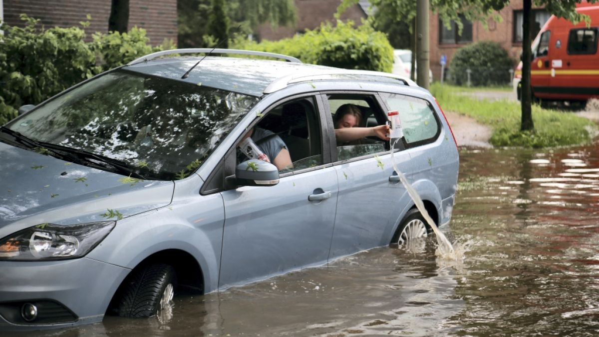 Fahrzeuginsassen kippen eingelaufenes Wasser aus ihrem Auto zurück auf die überflutete Straße in Hamburg-Bergedorf. (Foto)