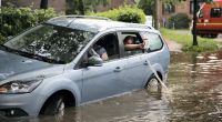 Fahrzeuginsassen kippen eingelaufenes Wasser aus ihrem Auto zurück auf die überflutete Straße in Hamburg-Bergedorf.