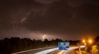 Die zahlreichen Blitze eines fernen Gewitters erhellen die dunklen Wolken über der Autobahn A661 im Nordosten von Frankfurt am Main.