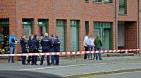Polizisten und Passanten stehen vor einem Haus in der Innenstadt von Neuss. Nach Schüssen ist eine 27-jährige Frau gestorben.