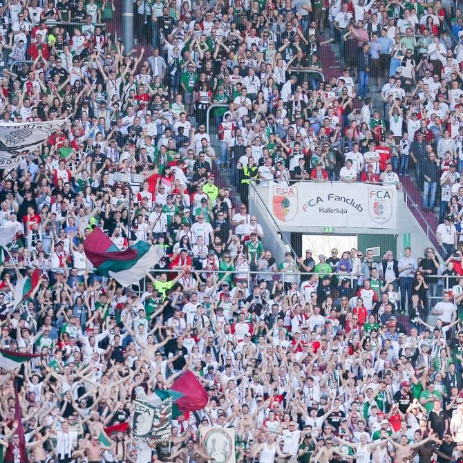 Die Fans des FC Augsburg stehen jubelnd hinter ihrer Mannschaft. (Symbolbild)