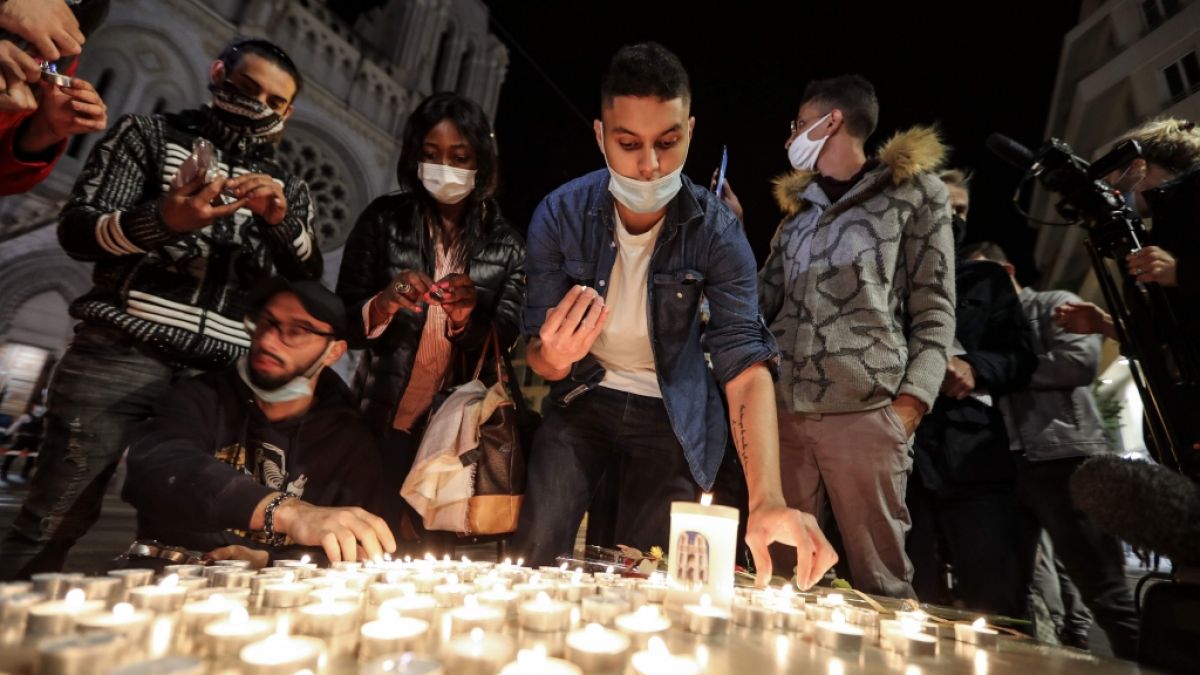 Menschen zünden Kerzen auf der Straße vor der Kirche Notre Dame für die Opfer einer Messerattacke an. (Foto)