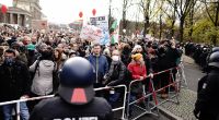 Teilnehmer einer Demonstration gegen die Corona-Einschränkungen der Bundesregierung stehen nach dem Brandenburger Tor an einer Absperrung Polizisten gegenüber.