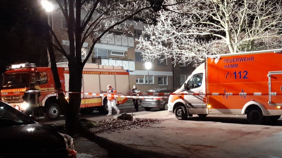 Ein Rettungswagen und ein Feuerwehrwagen stehen an dem mit einem Absperrband der Polizei abgesperrten Tatort auf einem Parkplatz in Hamm (NRW), an dem die Leiche einer 22-jährigen Frau gefunden wurde. (Foto)