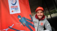 Johannes Rydzek, deutscher Nordischer Kombinierer, steht neben der offiziellen Fahne der Nordischen Ski-WM 2021.