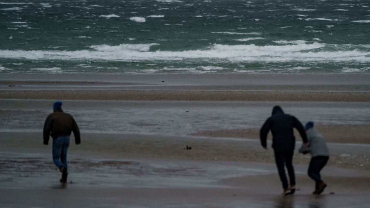 Spaziergänger stemmen sich gegen Windböen vor dem vom Wind aufgepeitschten Wasser am Ostsee-Strand. Der Deutsche Wetterdienst DWD warnte vor Sturm am Wochenende. (Foto)