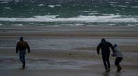 Spaziergänger stemmen sich gegen Windböen vor dem vom Wind aufgepeitschten Wasser am Ostsee-Strand. Der Deutsche Wetterdienst DWD warnte vor Sturm am Wochenende.