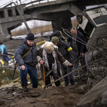 Örtliche Milizionäre helfen einer alten Frau über eine von Artillerie zerstörte Brücke am Stadtrand von Kiew.