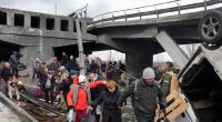 Menschen überqueren einen improvisierten Weg unter einer zerstörten Brücke auf der Flucht aus der Stadt Irpin in der Nähe von Kiew.