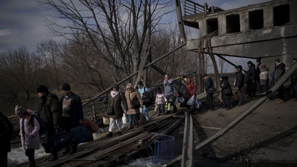Ukrainer überqueren einen improvisierten Weg unter einer zerstörten Brücke auf der Flucht vor russischen Angriffen aus Irpin, am Stadtrand von Kiew, Ukraine. (Foto)