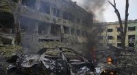 Ein Auto brennt neben einer durch einen Angriff beschädigten Geburtsklinik in Mariupol.