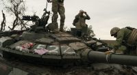 Ukrainische Soldaten stehen auf einem zerstörten russischen Panzer in der Region Charkiw.