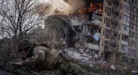Ein ukrainischer Polizist geht vor einem brennenden Gebäude in Awdijiwka in Deckung, das bei einem Luftangriff getroffen wurde.