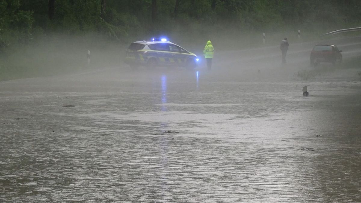 Ein Polizist und ein Fahrzeugfahrerstehen an einer überfluteten Strasse bei Detmold. (Foto)