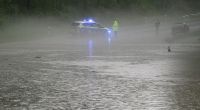 Ein Polizist und ein Fahrzeugfahrerstehen an einer überfluteten Strasse bei Detmold.