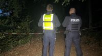 Polizisten stehen an einem abgesperrten Waldstück zwischen Halle-Kölkebeck und Hesselteich, einem Ortsteil von Versmold. Spaziergänger hatten in dem Waldstück im Kreis Gütersloh eine Leiche gefunden.