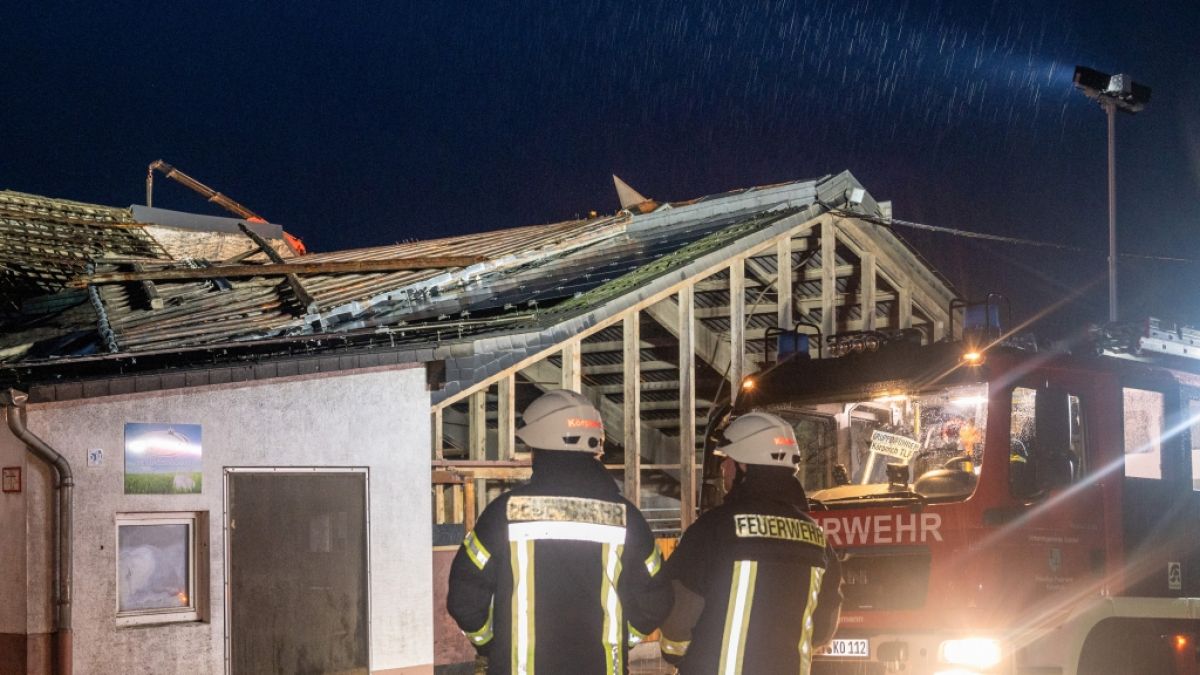 Einsatzkräfte der Freiwilligen Feuerwehr stehen vor einem Wirtschaftsgebäude, dessen Dacheindeckung fehlt. (Foto)