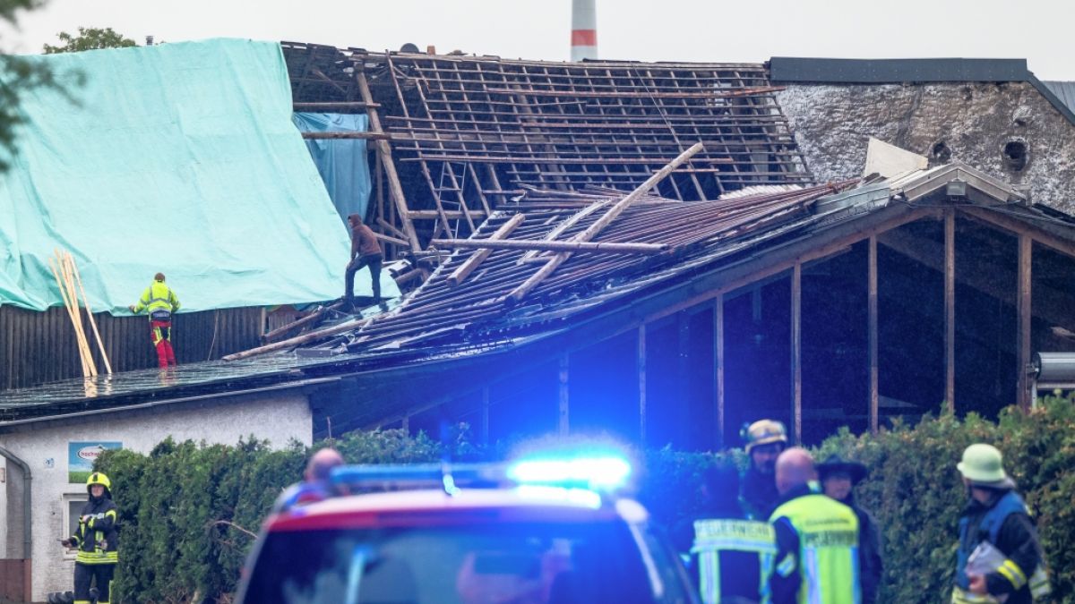Einsatzkräfte sichern das zerstörte Dach eines Hauses mit Planen gegen das Wetter während Feuerwehrleute sich vor einem zerstörten Haus beraten. (Foto)