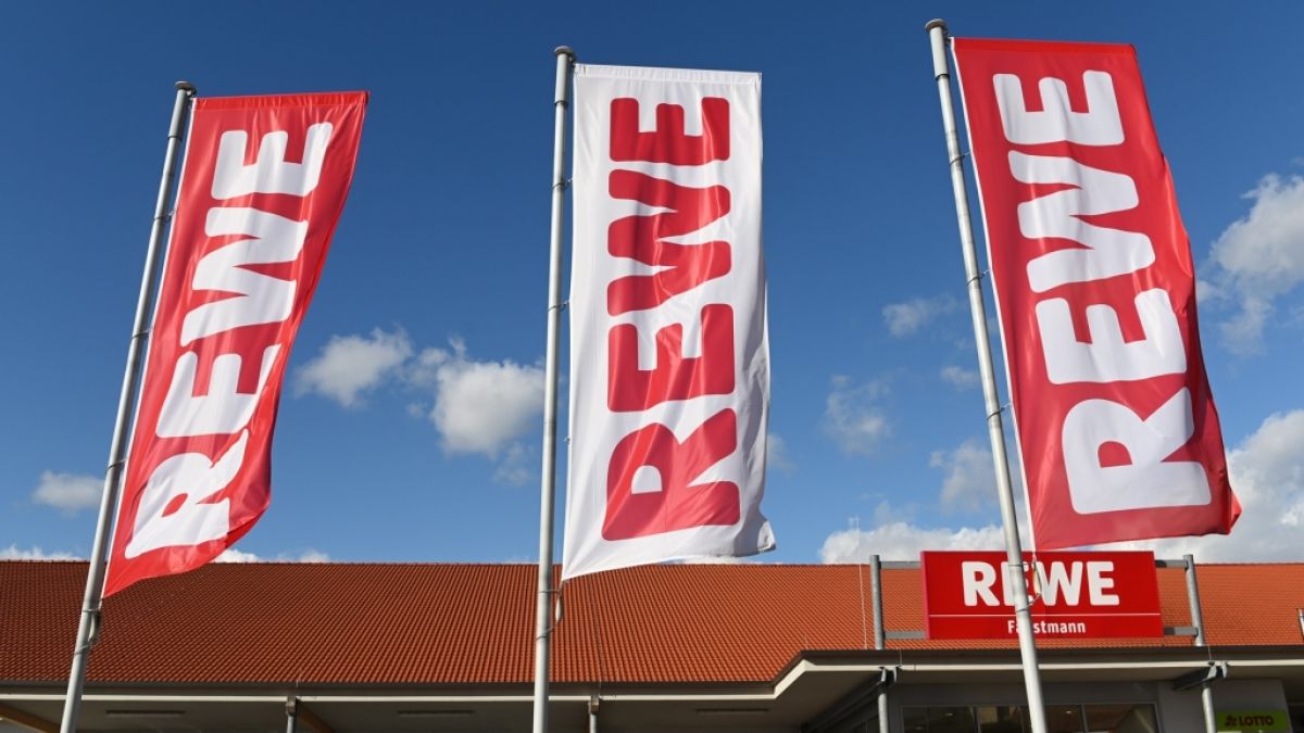 Fahnen mit dem REWE-Logo wehen vor einer Filiale des Einzelhändlers (Symbolbild). (Foto)