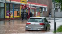 Passanten stapfen und fahren durch das Hochwasser in der Fischbachstrasse in Saarbrücken. Nach starken Regenfällen steht diese teilweise unter Wasser.