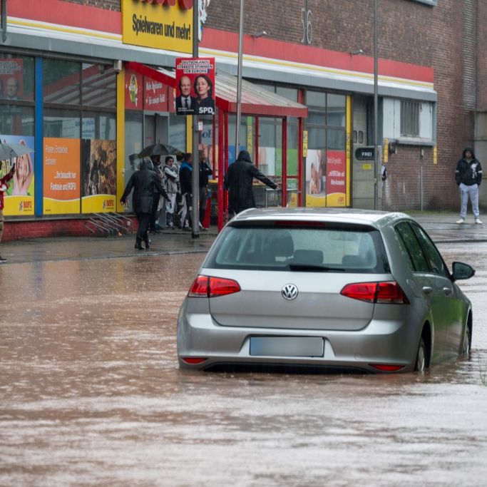 Passanten stapfen und fahren durch das Hochwasser in der Fischbachstrasse in Saarbrücken. Nach starken Regenfällen steht diese teilweise unter Wasser.