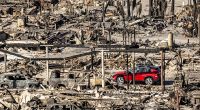 Ein rotes Auto fährt an Häusern und Fahrzeugen vorbei, die durch das Palisades-Feuer in den Pacific Palisades Bowl Mobile Estates zerstört wurden.