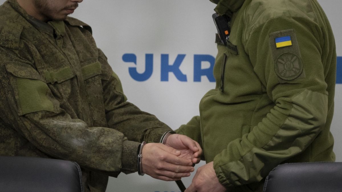 Ein ukrainischer Sicherheitsbeamter (r.) eskortiert einen in Handschellen geführten Chinesen (l.), der in Donezk gefangen genommen wurde, zu einer Pressekonferenz in Kiew. (Foto)